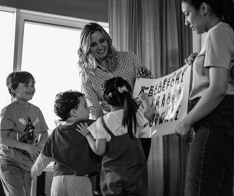 Two teachers working with young children, showing them an alphabet poster